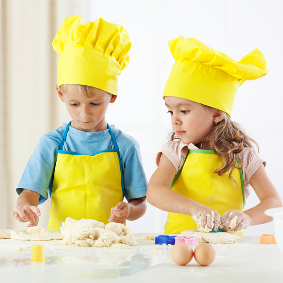 Two kids cooking wearing yellow aprons and chef's hats