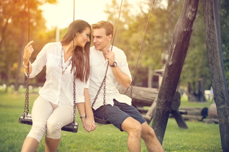 Male and female lean towards each other on swings