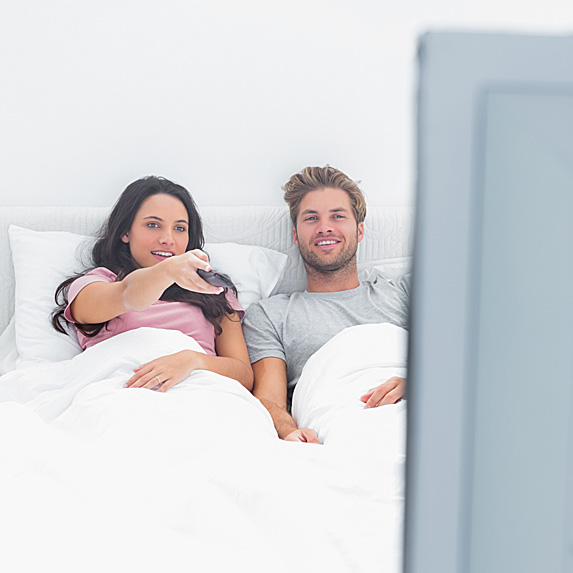 A couple laughing and watching TV from bed.