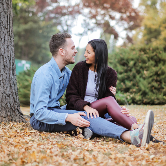 Young mixed race couple laughing and cuddling under a tree