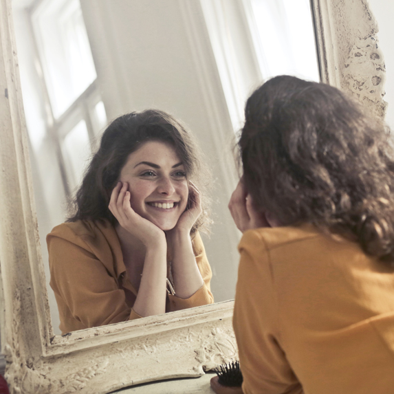 Woman wearing light makeup looking at herself in mirror