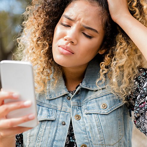 Upset woman holding her head while looking at her phone