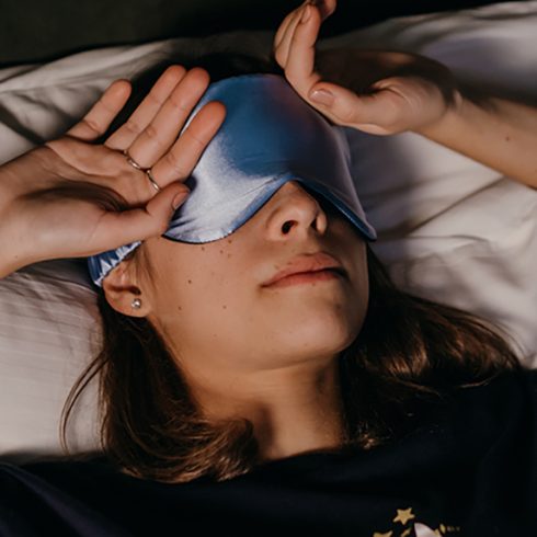 a white woman lying in bed with a sleep mask on