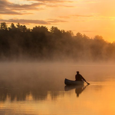 Silhouette of a canoe on a lake, water reflecting the golden light above