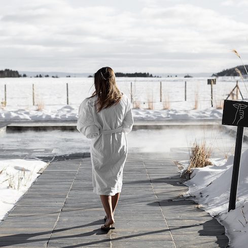 Woman in a robe walks towards an outdoor spa facility at Spa Nordique