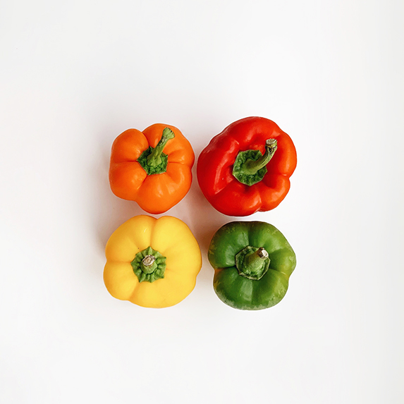four bell peppers - orange, red, yellow and green - against a white background