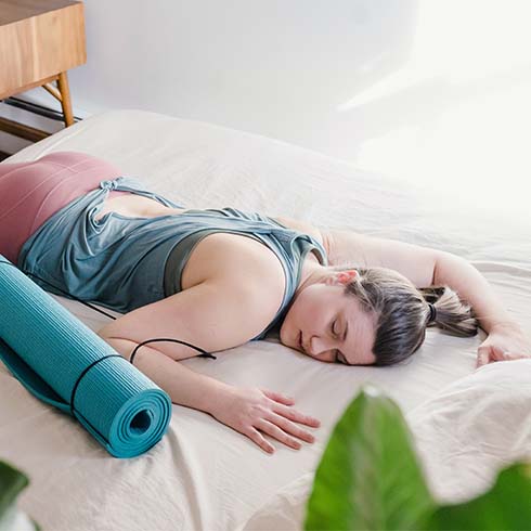 woman laying on bed bedisde yoga mat
