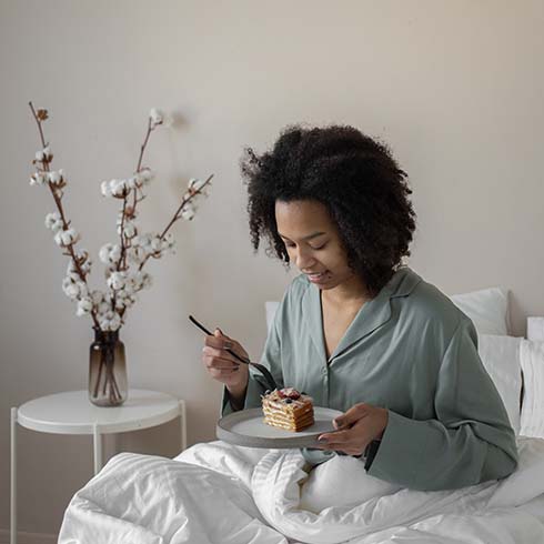 Black woman eating a snack in comfy bed