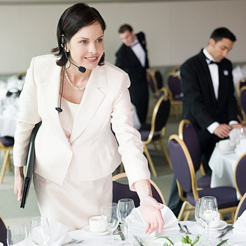 A wedding planner in a suit looks over a table in preparation for a wedding.