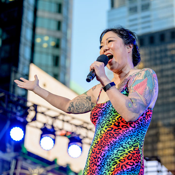 Margaret Cho performs in a rainbow striped dress, with her black hair tied back