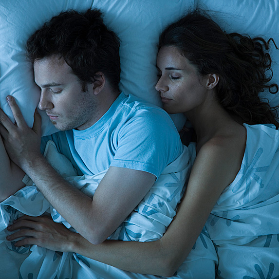 Man and woman sleeping in bed, with woman spooning the man