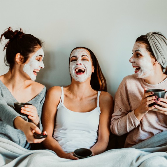 three women laughing while watching television