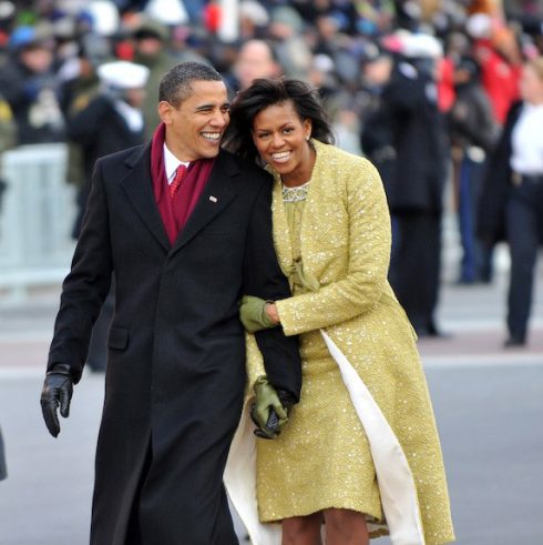 Barack and Michelle Obama walking in winter coats and leaning on each other, laughing