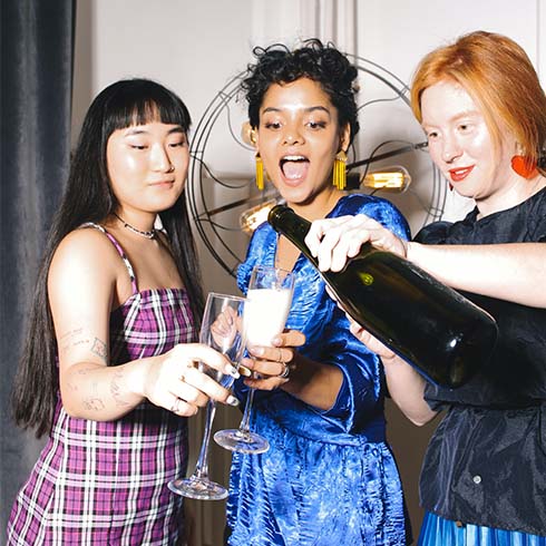 Three young women pouring champagne into glasses.