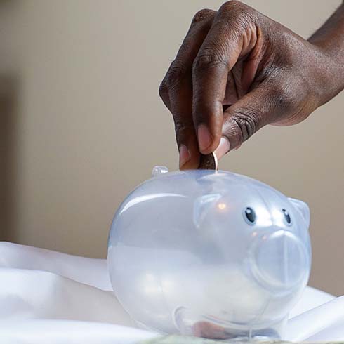 Black hand putting coin in piggy bank