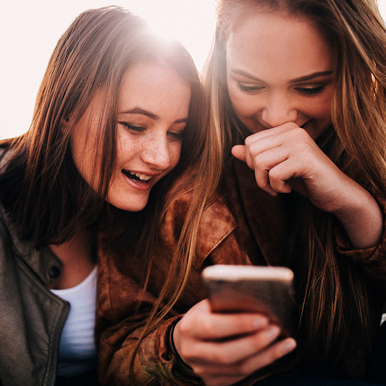 two young white women laughing while looking at a cell phone