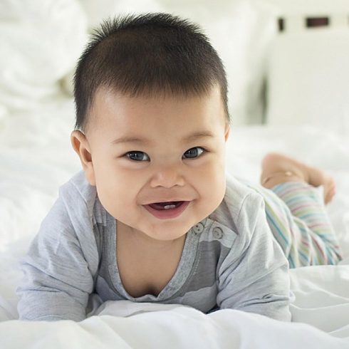 Smiling Asian baby boy on his tummy.