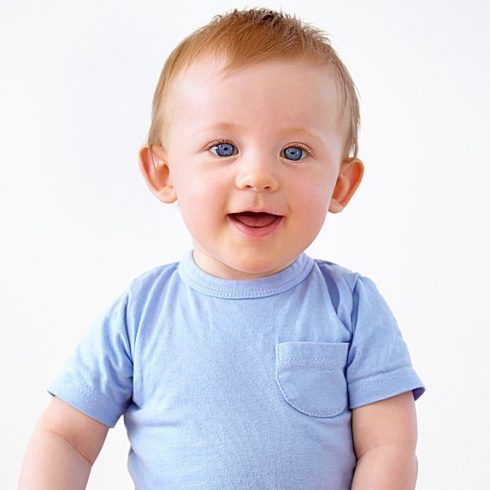 A red-haired baby both with blue eyes and a blue shirt smiling at the camera.
