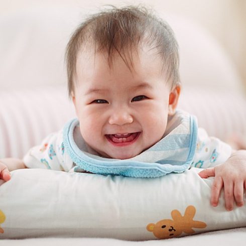 Laughing Asian baby with a wide grin and baby teeth showing