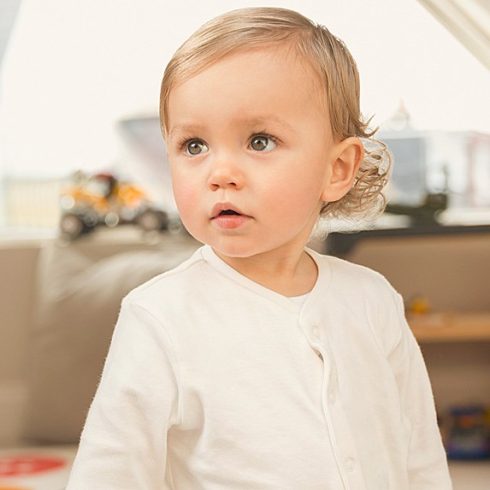 Blonde, hazel-eyed baby boy with longish hair and a white shirt looking off-camera