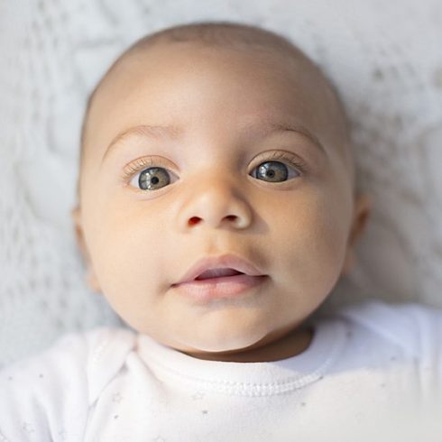 Sweet bi-racial baby with light eyes and very short hair looking up at the camera