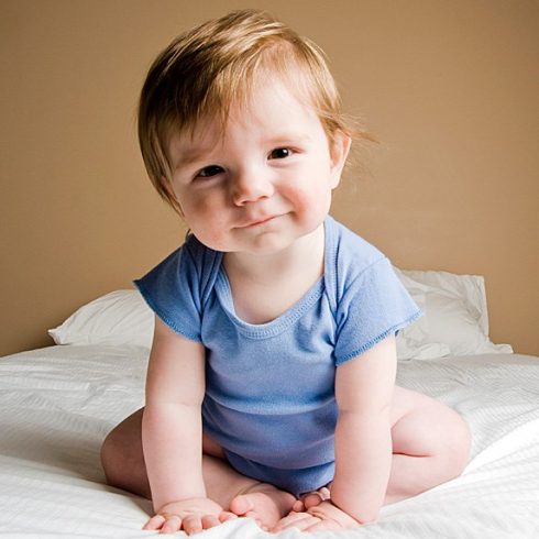 Smiling baby sitting with tipped head and strawberry-blonde hair