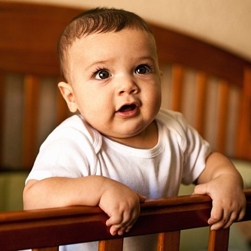Chubby baby boy looking out from his crib