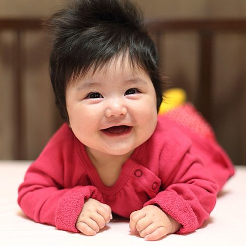 Smiling Asian baby on tummy in a coral robe.