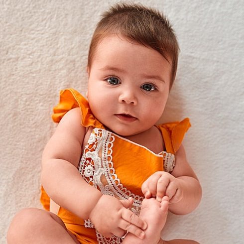 Brown-haired, blue-eyed white baby in an orange outfit laying on its back.