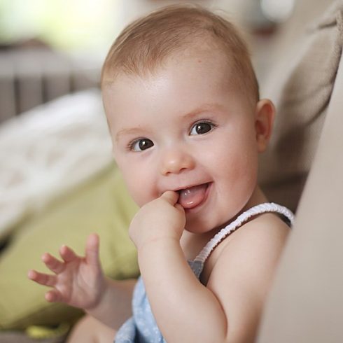 Smiling white baby chewing her finger