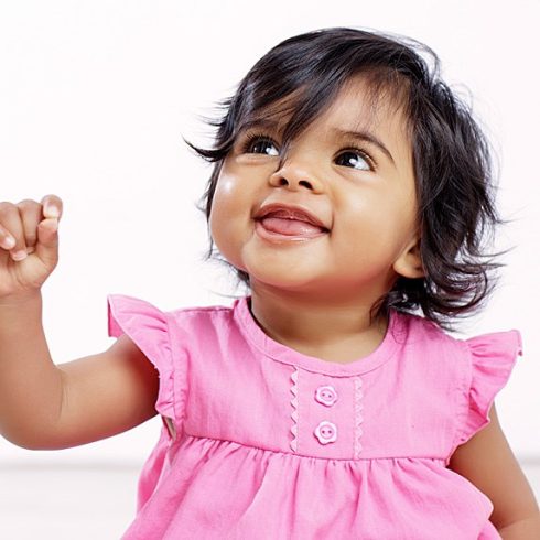 South-East Asian baby girl in a pink dress smiling, off-camera
