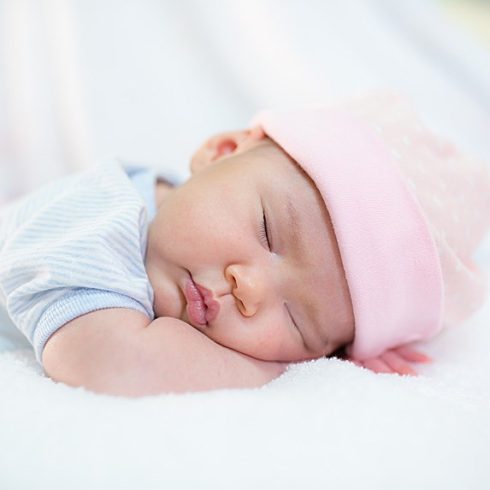 Asian baby sleeping on her forearm in a light pink hat