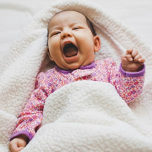 Yawning Asian baby on her back