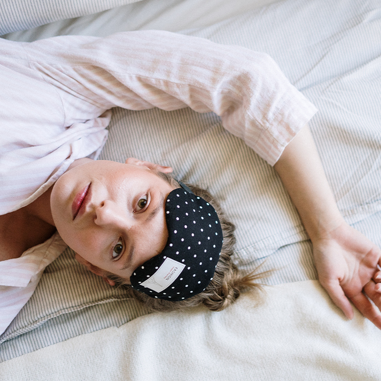 Girl laying in bed with sleep mask raised above her eyes looking restless