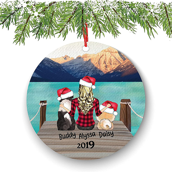Custom ornament with a woman and two dogs sitting on the doc of a bay