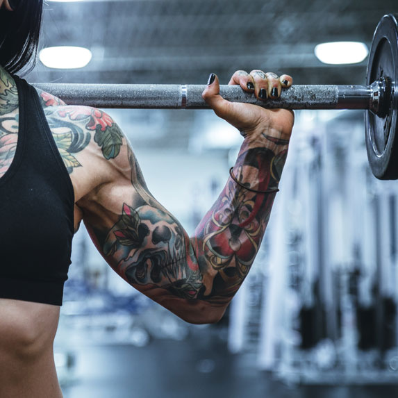 A close-up of a tattooed woman lifting weights
