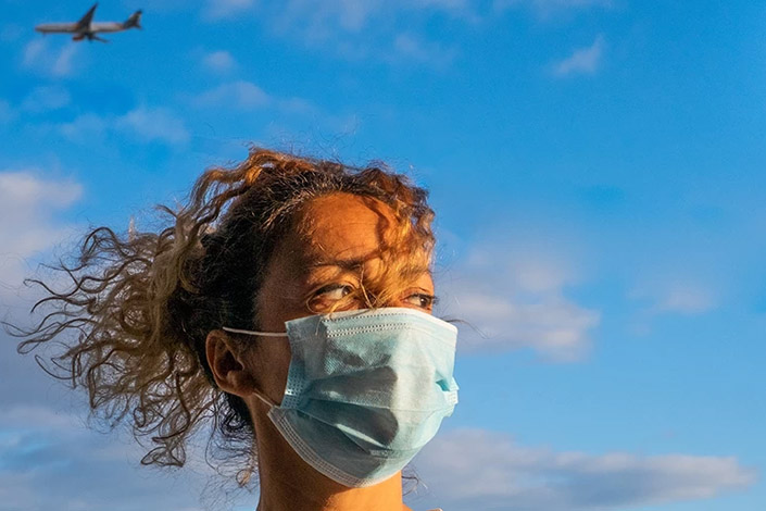 Woman wearing PPE mask with airplane flying in the sky behind her