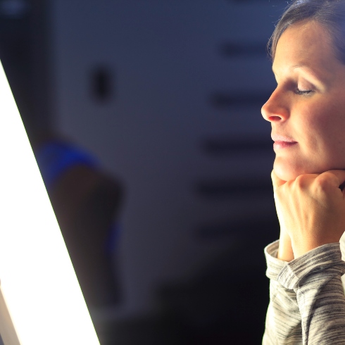 A woman sitting in front of a light therapy device resting her chin on her hands