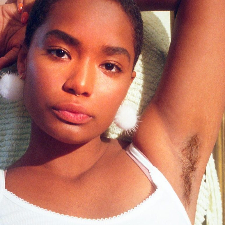 Attractive black woman wearing a tank top with her arms above her head revealing underarm hair.