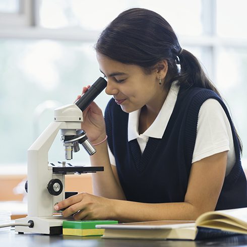 Young hispanic girl looking into a microscope at school.