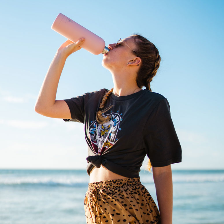 A woman by water drinking out of a pink water bottle