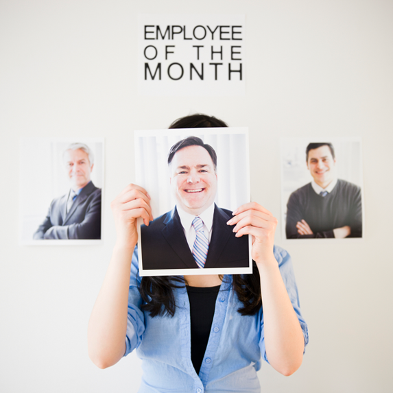 Woman standing in front of Employee of the Month wall holding picture of a man over her face