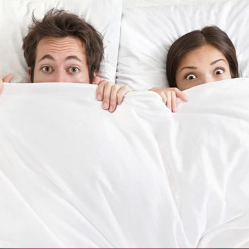 Man and woman look surprised with the sheets over half their faces