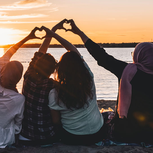 Four women making heart signs with their hands in the warmth of the sunset
