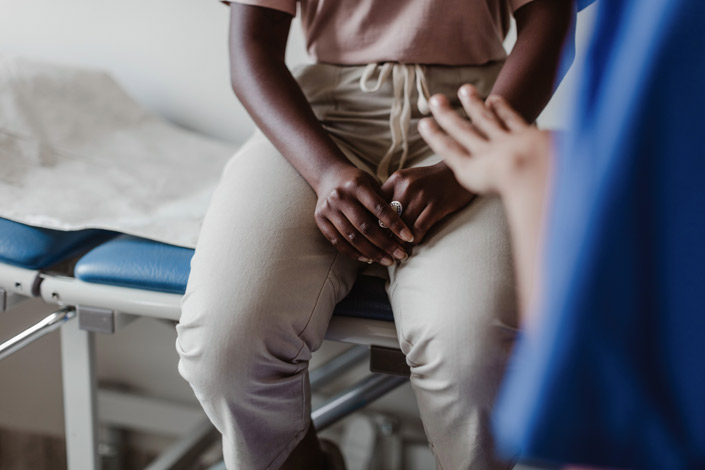 Black woman with hands together in a doctor's office, showing the waist down.
