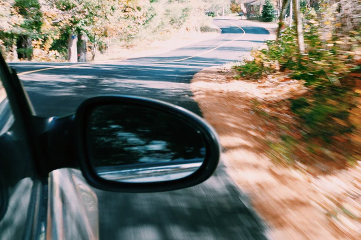 view of side mirror of a car as it drives down a windy road
