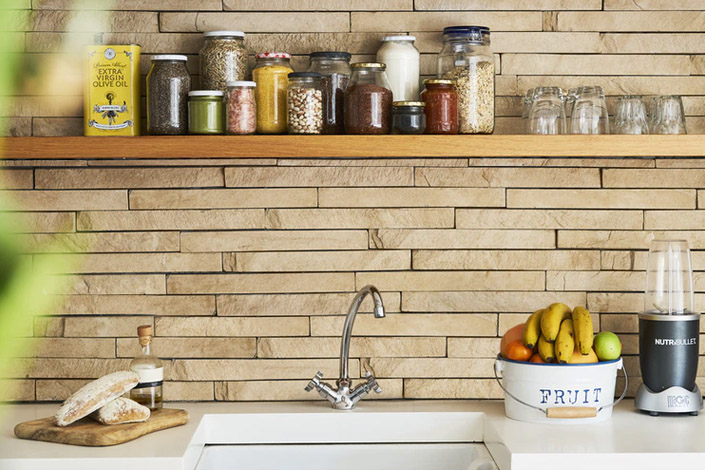 Cute kitchen featuring sink with wooden backsplash and shelf with many jars