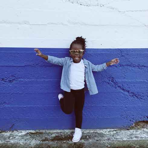 A happy little girl on her own posing against a wall.