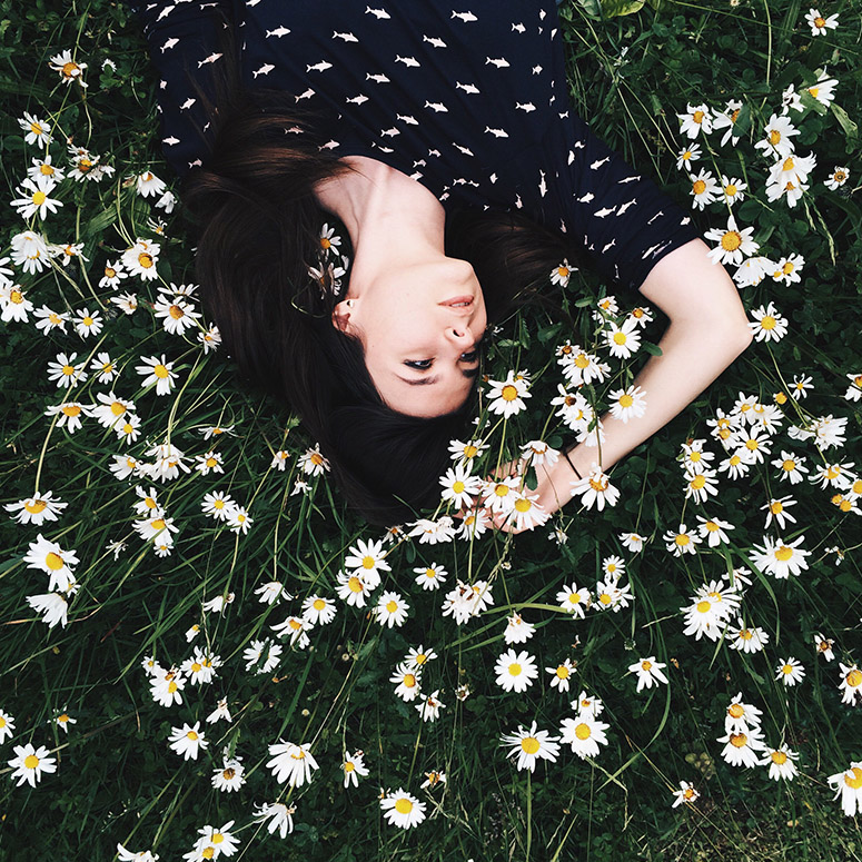 Woman lies in a field of white flowers touching them with one hand while upside down
