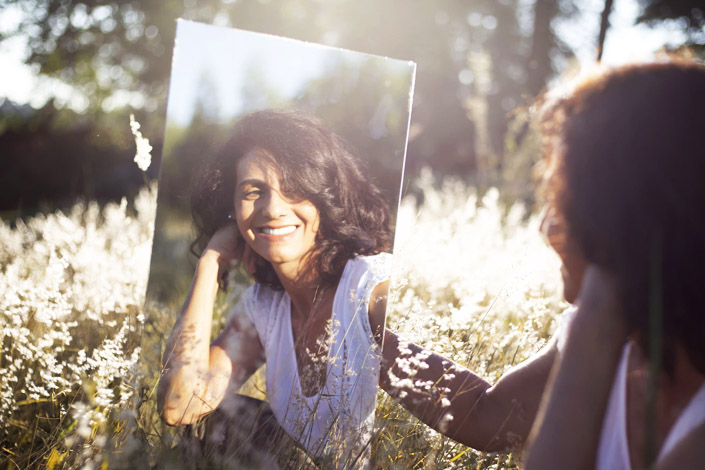 Woman holding a mirror up to herself in a field